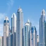 Dubai Marina skyline with modern glass towers and the twisted Cayan Tower under a clear blue sky