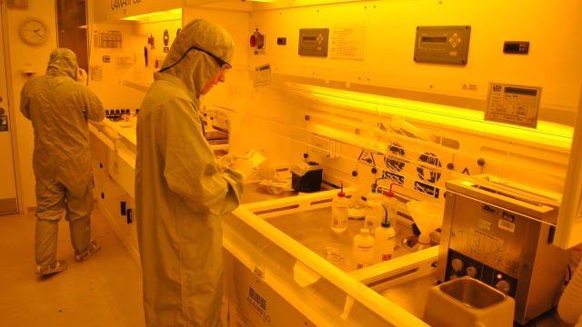 Technicians in cleanroom suits working at photolithography stations under yellow safelight